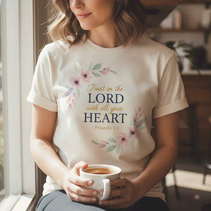 Woman sitting in a cozy café wearing an ivory Comfort Colors Christian t-shirt with pink floral design and scripture “Trust in the Lord with all your heart – Proverbs 3:5,” holding a warm cup of coffee near a window