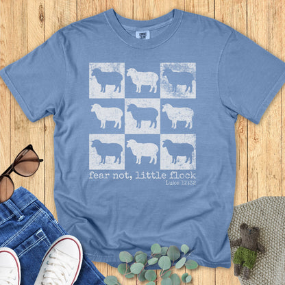 Comfort Colors 1717 Christian women t-shirt in blue jean color with distressed 3x3 sheep illustration and Bible verse "fear not, little flock – Luke 12:32," shown on a flat lay setup with casual outfit pieces