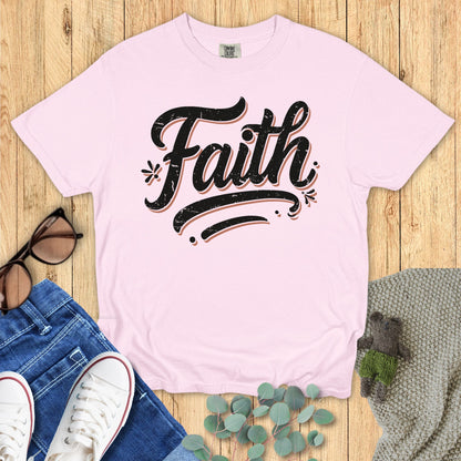 Comfort Colors 1717 pink “Faith” t-shirt with bold distressed typography, displayed with jeans and cozy accessories. A modern Christian shirt that’s part of the faith-based apparel for women collection.