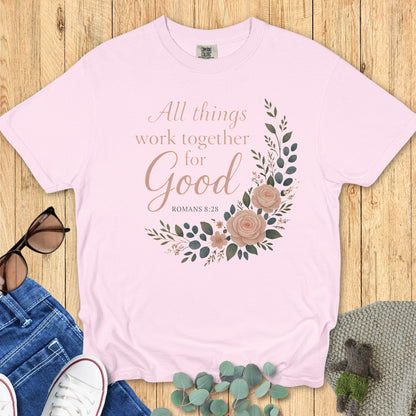 Flatlay of a Comfort Colors 1717 blossom pink “All Things Work Together for Good – Romans 8:28” t-shirt featuring blush floral illustration. A feminine design from faith-based apparel for women, perfect as a Christian mom gift idea.