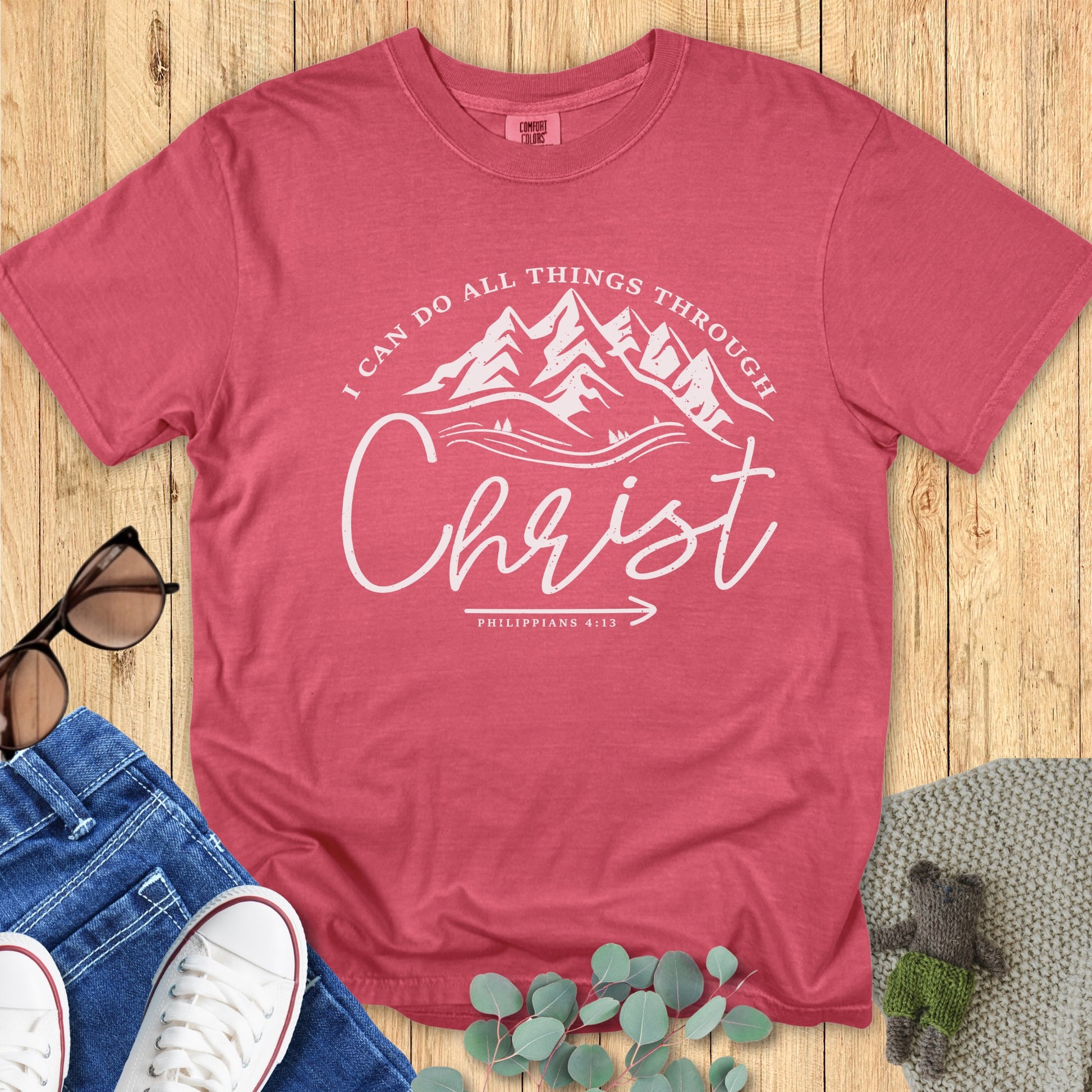Flatlay of a Comfort Colors 1717 crimson “I Can Do All Things Through Christ – Philippians 4:13” t-shirt featuring mountain line art. A strong and uplifting women’s scripture tee reminding believers of God’s strength.