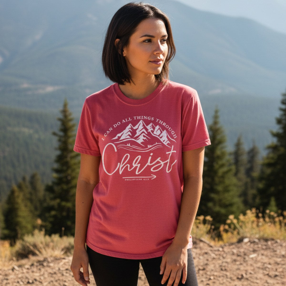 Woman standing in a mountain landscape wearing a Comfort Colors 1717 crimson “I Can Do All Things Through Christ – Philippians 4:13” t-shirt. A bold women’s scripture tee for faith-filled adventure and encouragement.