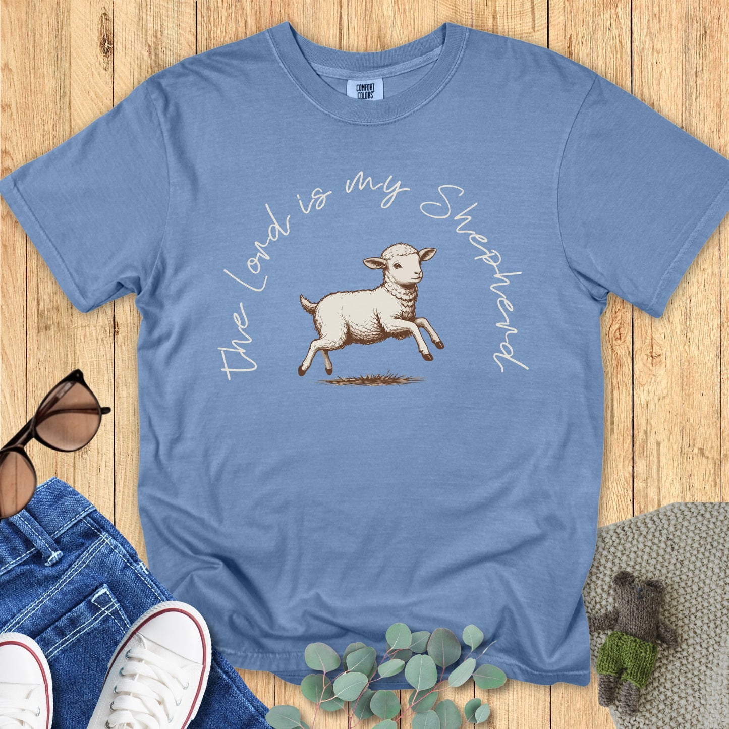 Flatlay of a Comfort Colors 1717 blue jean “The Lord Is My Shepherd” t-shirt styled with jeans and accessories. A gentle and meaningful women’s scripture tee that makes a thoughtful Christian mom gift idea.