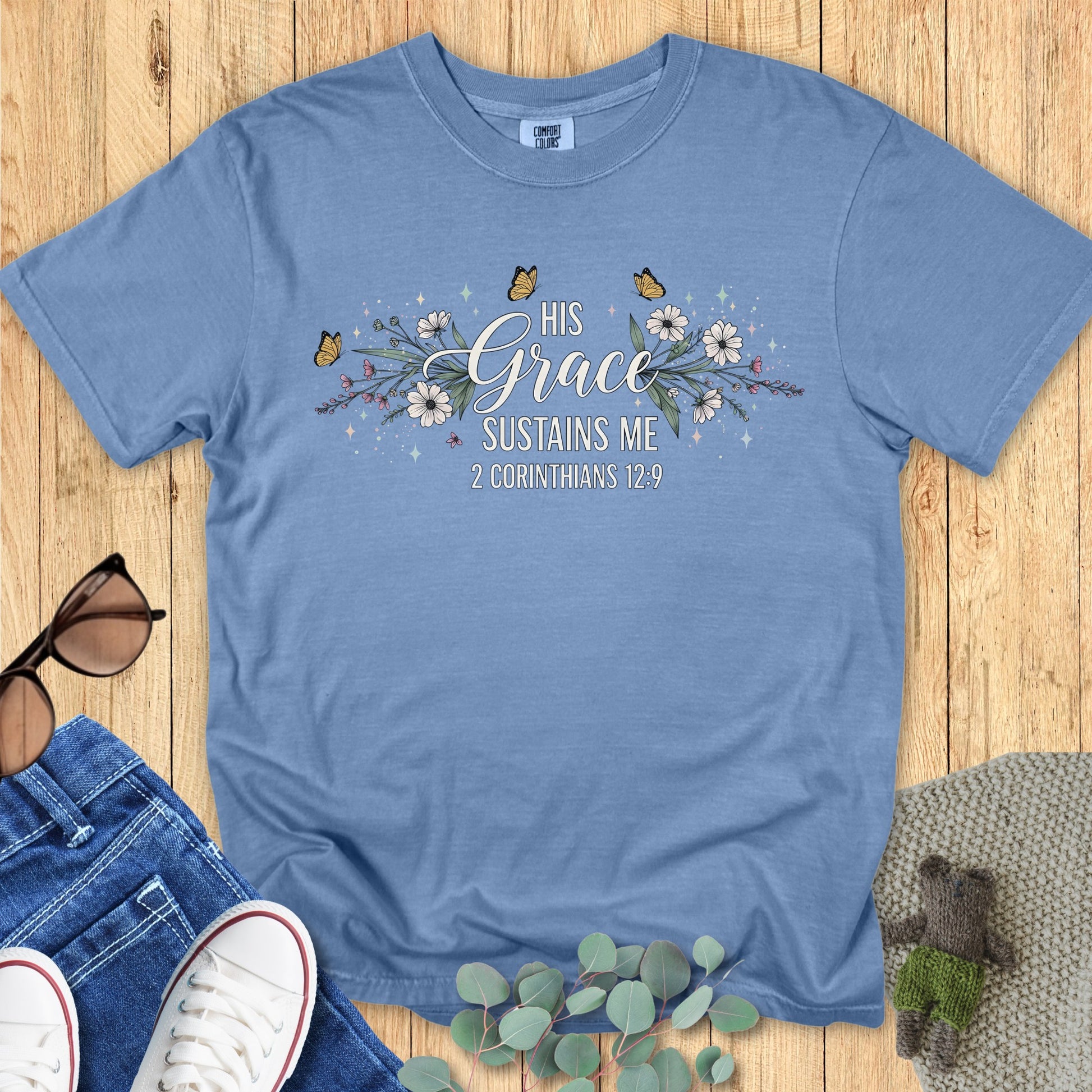 Comfort Colors 1717 blue jean “His Grace Sustains Me – 2 Corinthians 12:9” t-shirt with floral and butterfly artwork. A stylish modern Christian shirt that reminds believers of God’s strength — perfect women’s scripture tee and faith-inspired gift.