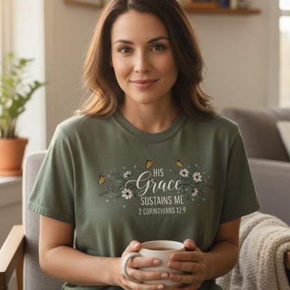 Peaceful woman enjoying coffee in a cozy home wearing a Comfort Colors 1717 moss “His Grace Sustains Me – 2 Corinthians 12:9” t-shirt. A serene and uplifting women’s scripture tee — beautiful modern Christian shirt and heartfelt Christian mom gift idea.