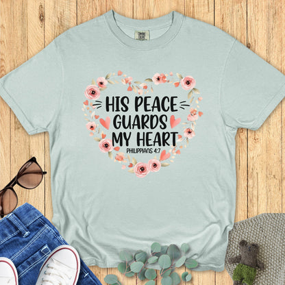 Flatlay of a Comfort Colors 1717 bay “His Peace Guards My Heart – Philippians 4:7” t-shirt featuring soft floral artwork forming a heart shape. A refreshing and serene piece of faith-based apparel for women — perfect Christian mom gift idea or devotional wear.
