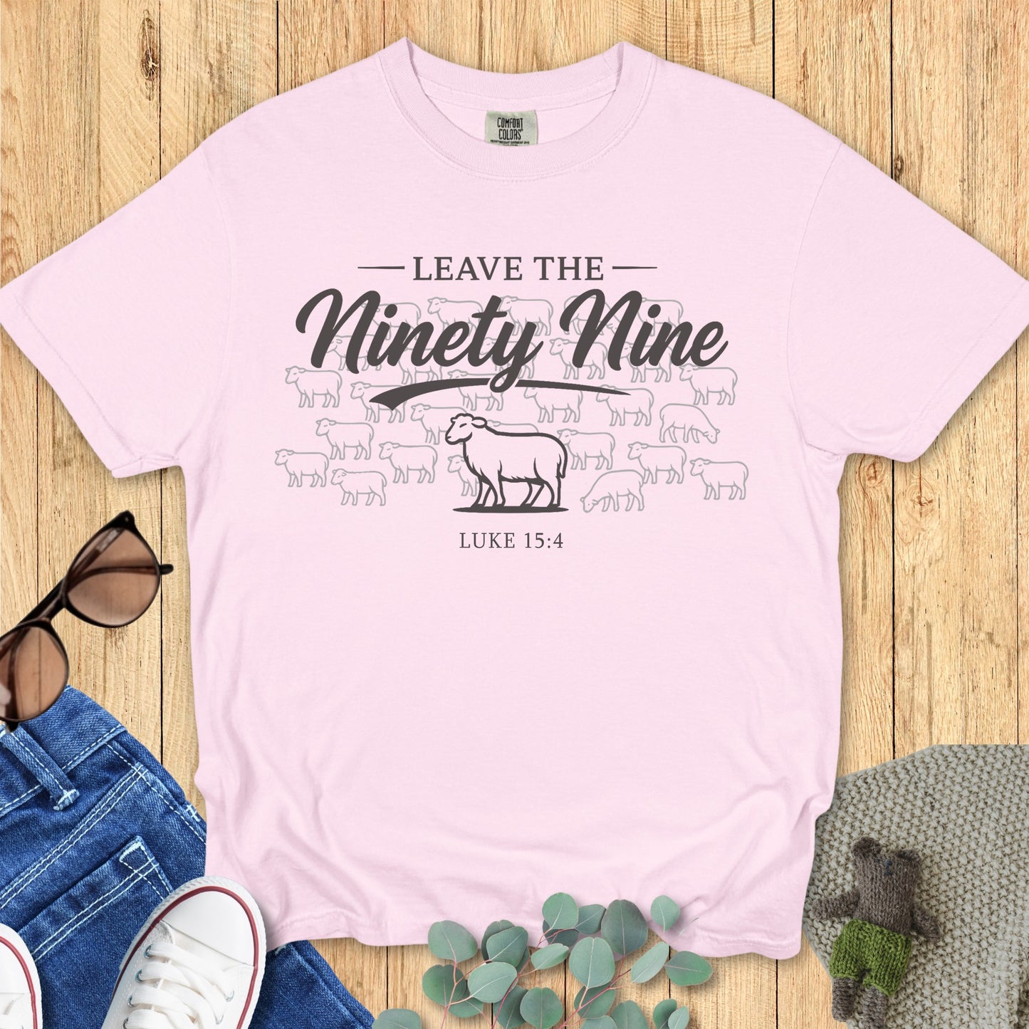 Flatlay of a Comfort Colors 1717 blossom “Leave the Ninety-Nine – Luke 15:4” t-shirt with a lost sheep illustration. A graceful and inspiring women’s scripture tee — faith-based apparel for women and meaningful Christian mom gift that celebrates Luke 15:4.