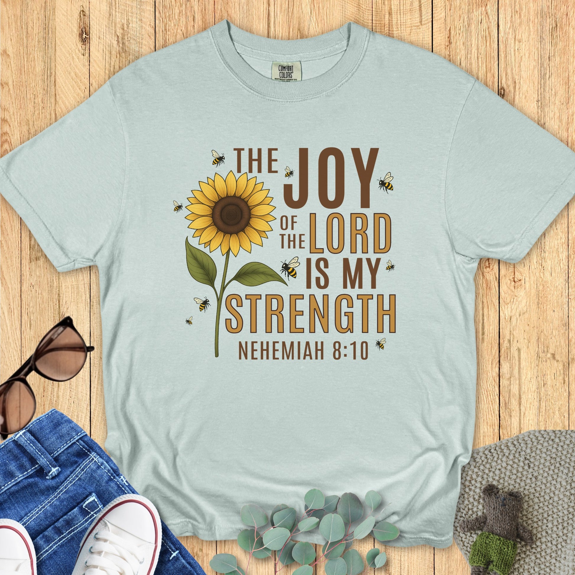 Comfort Colors 1717 bay “The Joy of the Lord Is My Strength – Nehemiah 8:10” t-shirt with sunflower and bee artwork. A refreshing women’s scripture tee — modern Christian shirt and faith-based apparel for women inspired by joy and strength in the Lord.