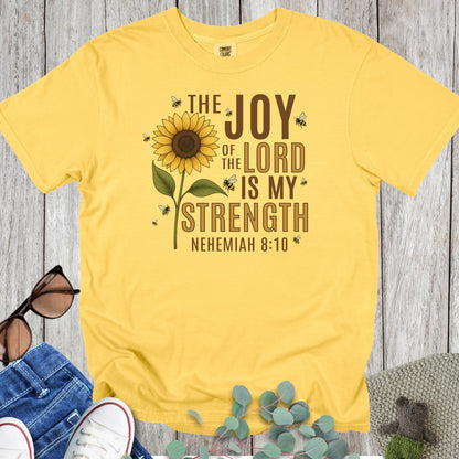 Flatlay of a Comfort Colors 1717 citrus “The Joy of the Lord Is My Strength – Nehemiah 8:10” t-shirt featuring a sunflower surrounded by bees. A radiant and joyful women’s scripture tee — bright faith-based apparel for women and thoughtful Christian mom gift.