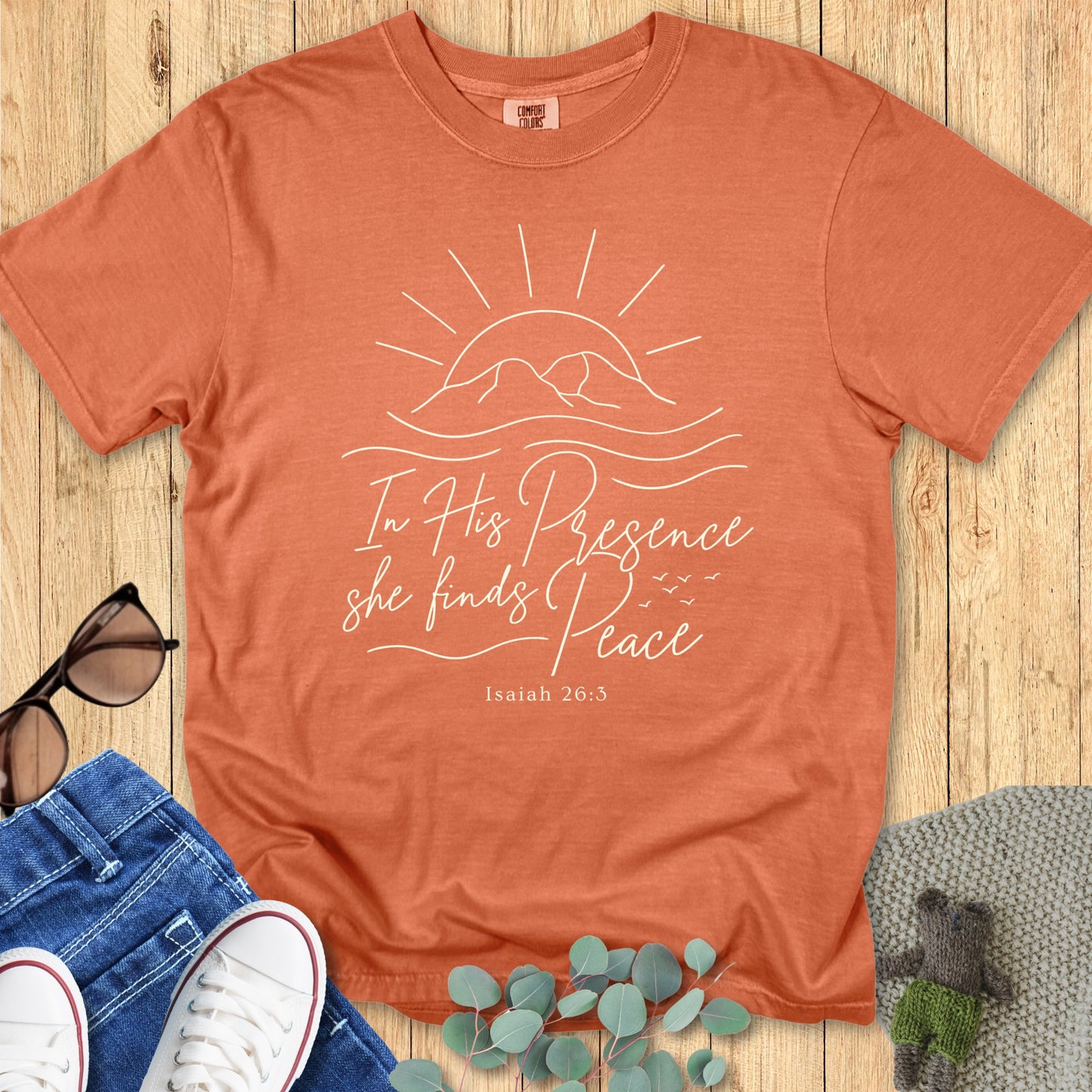 Flatlay of a Comfort Colors 1717 yam “In His Presence She Finds Peace – Isaiah 26:3” t-shirt with minimalist sun and waves line art. A warm and soothing women’s scripture tee — faith-based apparel for women and modern Christian shirt, ideal Christian mom gift idea.