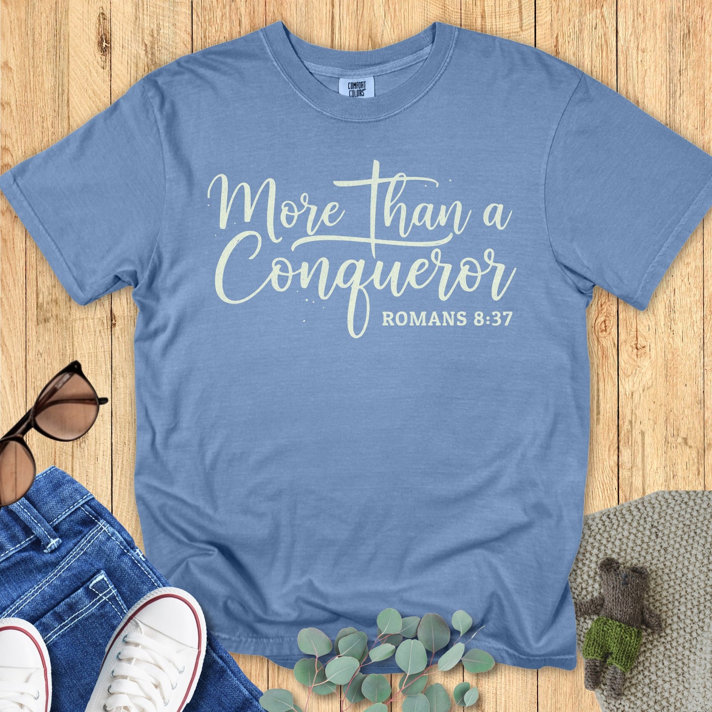 Comfort Colors 1717 blue jean “More Than a Conqueror – Romans 8:37” t-shirt with creamy white text in cursive script. A stylish women’s scripture tee — empowering faith-based apparel for women and encouraging modern Christian shirt, ideal for Christian mom gift ideas.