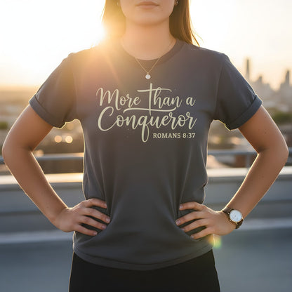 Woman standing outdoors at sunset wearing a Comfort Colors 1717 pepper “More Than a Conqueror – Romans 8:37” t-shirt. A confident women’s scripture tee — modern Christian shirt and faith-based apparel for women, making an empowering Christian mom gift idea.