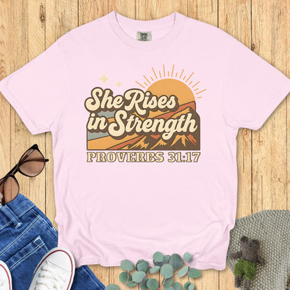 Comfort Colors 1717 blossom “She Rises in Strength – Proverbs 31:17” t-shirt in pastel pink with retro mountain sunrise artwork. A feminine women’s scripture tee — inspiring faith-based apparel for women and thoughtful Christian mom gift idea.