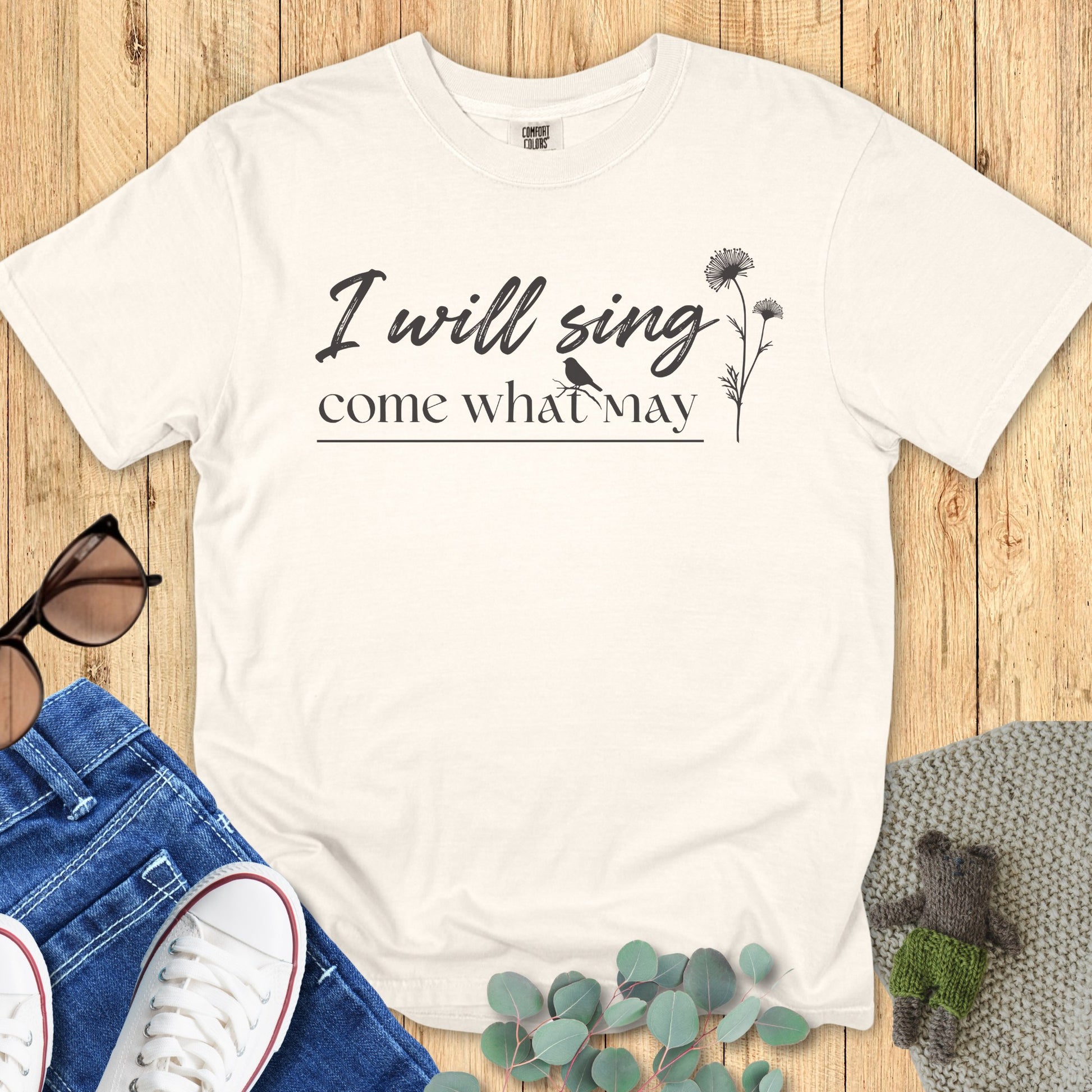latlay of a Comfort Colors 1717 ivory “I Will Sing Come What May” t-shirt featuring elegant black script and hand-drawn floral details. A timeless women’s scripture tee — modern faith-based apparel for women and meaningful Christian mom gift idea.