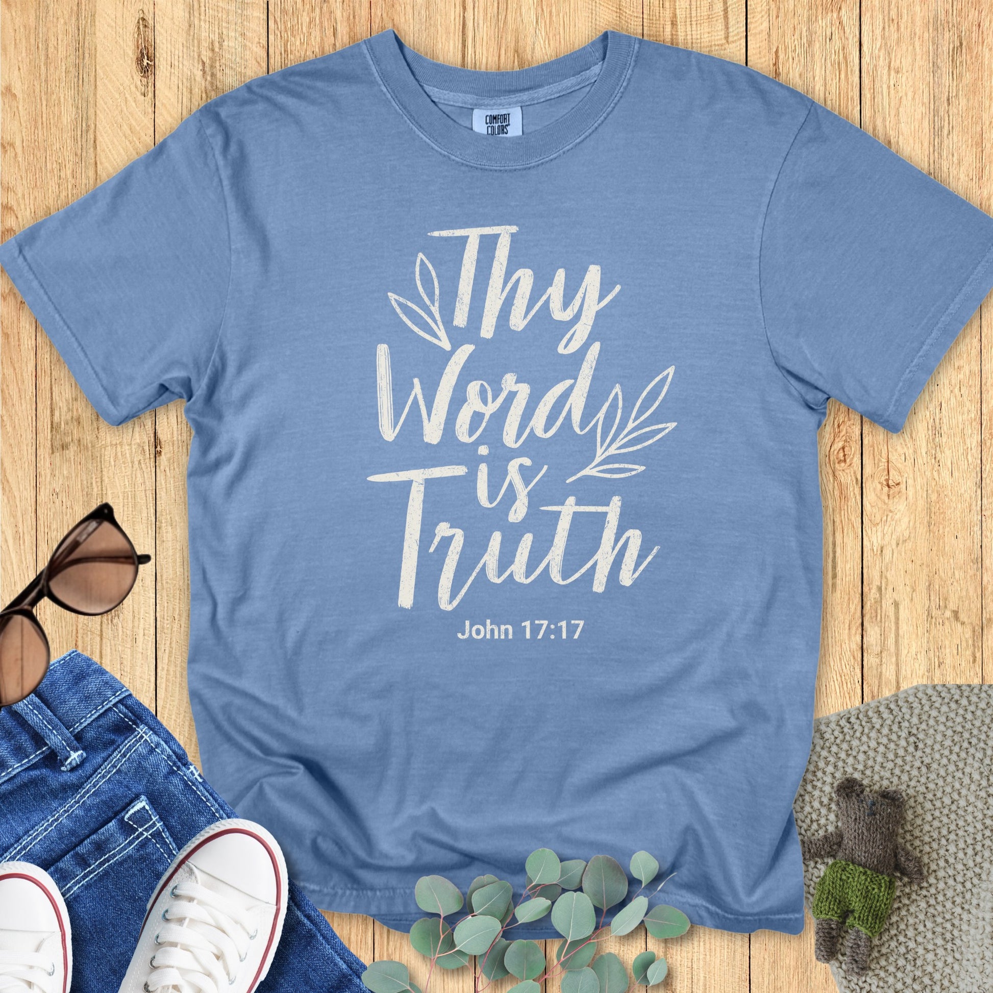 Flatlay of a Comfort Colors 1717 blue jean “Thy Word Is Truth – John 17:17” t-shirt featuring cream lettering and simple leaf design. A beautiful women’s scripture tee — uplifting faith-based apparel for women and stylish modern Christian shirt, great Christian mom gift idea.