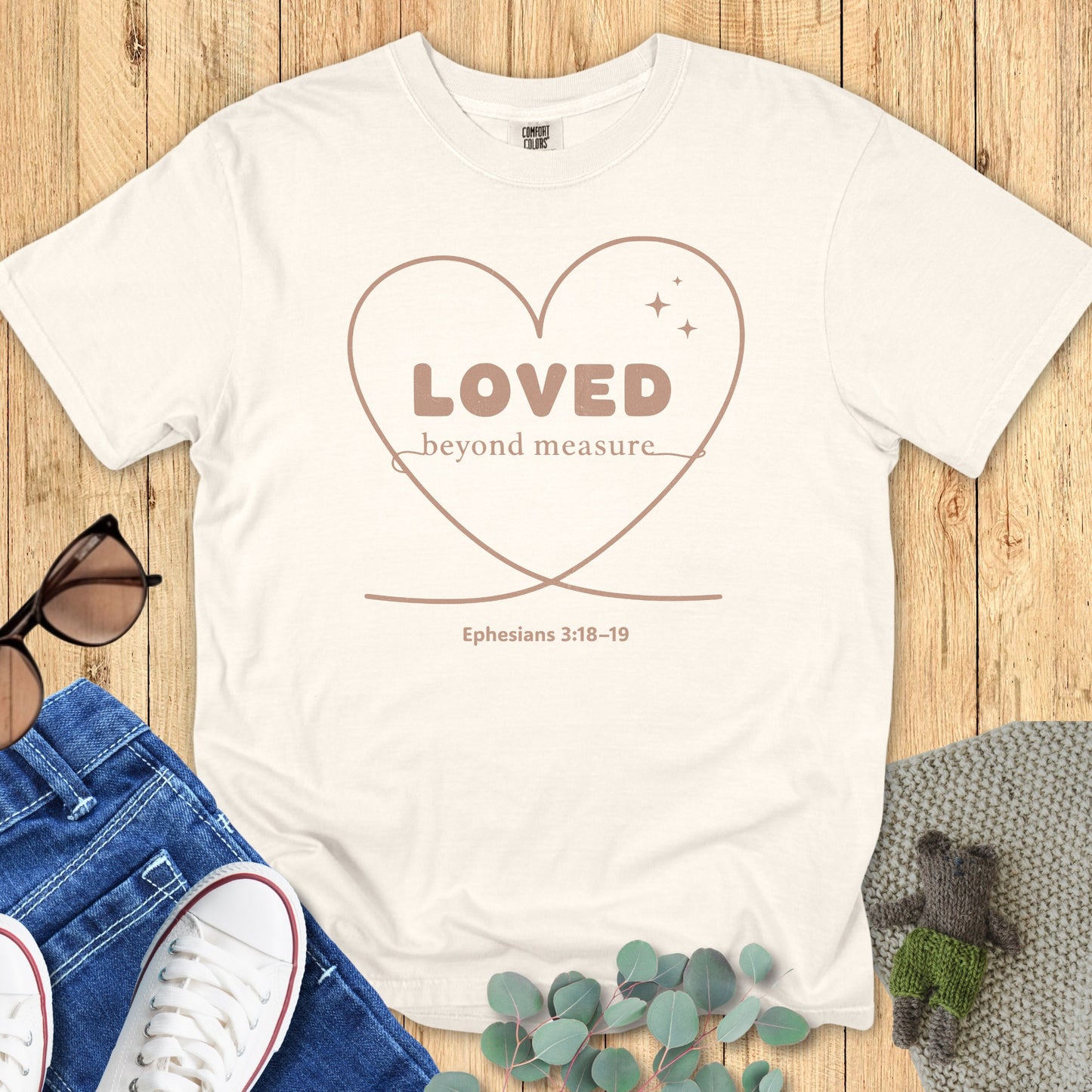 Flatlay of a Comfort Colors 1717 ivory “Loved Beyond Measure – Ephesians 3:18-19” t-shirt featuring minimalist heart artwork and elegant lettering. A classic women’s scripture tee — uplifting faith-based apparel for women and modern Christian shirt, lovely Christian mom gift idea.