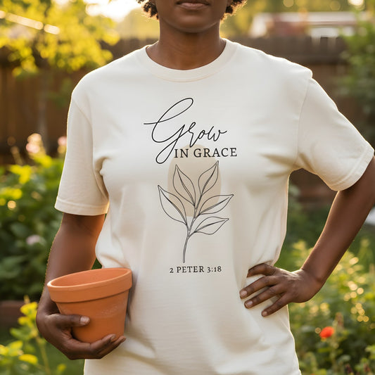 Woman standing in a sunny garden holding a clay pot while wearing a Comfort Colors 1717 ivory “Grow in Grace – 2 Peter 3:18” t-shirt with minimalist botanical line art. A serene women’s scripture tee — elegant faith-based apparel for women and modern Christian shirt, thoughtful Christian mom gift idea.