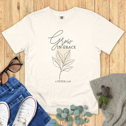 Flatlay of a Comfort Colors 1717 ivory “Grow in Grace – 2 Peter 3:18” t-shirt featuring a simple leaf design and modern script typography. A peaceful women’s scripture tee — uplifting faith-based apparel for women and modern Christian shirt, ideal Christian mom gift idea.