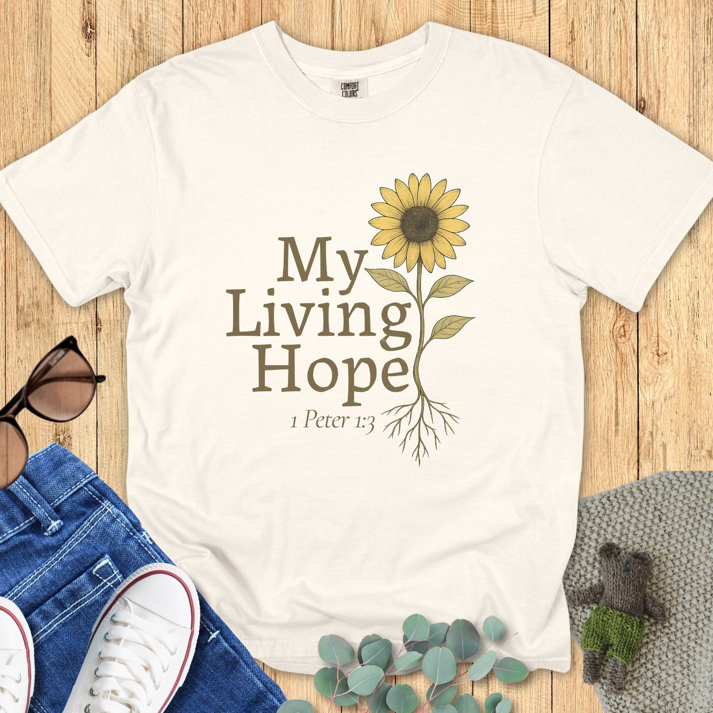 Flatlay of a Comfort Colors 1717 ivory “My Living Hope – 1 Peter 1:3” t-shirt with hand-drawn sunflower and rooted design. A beautiful women’s scripture tee — faith-based apparel for women and modern Christian shirt, perfect Christian mom gift idea.