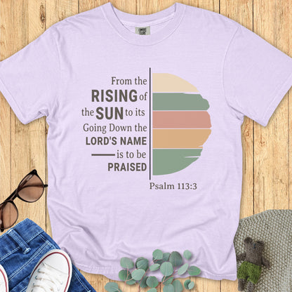 Flatlay of a Comfort Colors 1717 orchid “From the Rising of the Sun to its Going Down, the Lord’s Name is to be Praised – Psalm 113:3” t-shirt with muted sunrise graphic. A soft and inspiring women’s scripture tee — faith-based apparel for women and modern Christian shirt, lovely Christian mom gift idea.