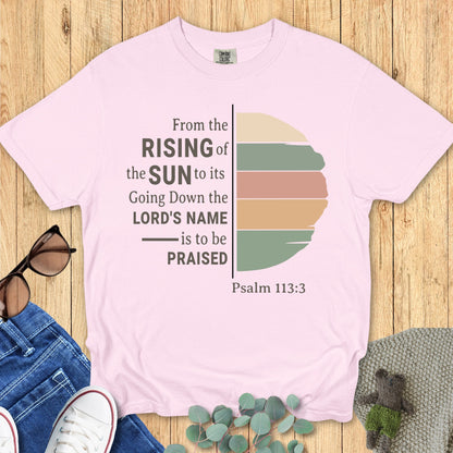 Flatlay of a Comfort Colors 1717 blossom “From the Rising of the Sun to its Going Down, the Lord’s Name is to be Praised – Psalm 113:3” t-shirt with vintage-style striped sun illustration. A feminine women’s scripture tee — faith-based apparel for women and modern Christian shirt, meaningful Christian mom gift idea.