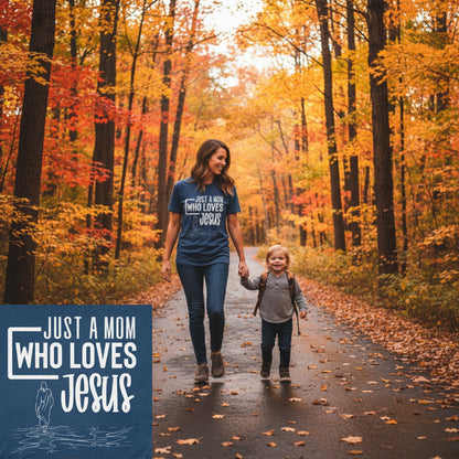 Mom walking with her child in the autumn woods wearing a Comfort Colors 1717 navy “Just a Mom Who Loves Jesus” t-shirt with a simple Jesus walking on water outline. A heartfelt women’s scripture tee — faith-based apparel for women and modern Christian shirt, perfect Christian mom gift idea.