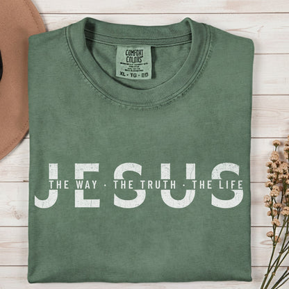 Comfort Colors 1717 moss “Jesus — The Way, The Truth, The Life” t-shirt styled with a hat and floral decor. A minimalist women’s scripture tee — faith-based apparel for women and modern Christian shirt with John 14:6 verse, perfect Christian mom gift idea.