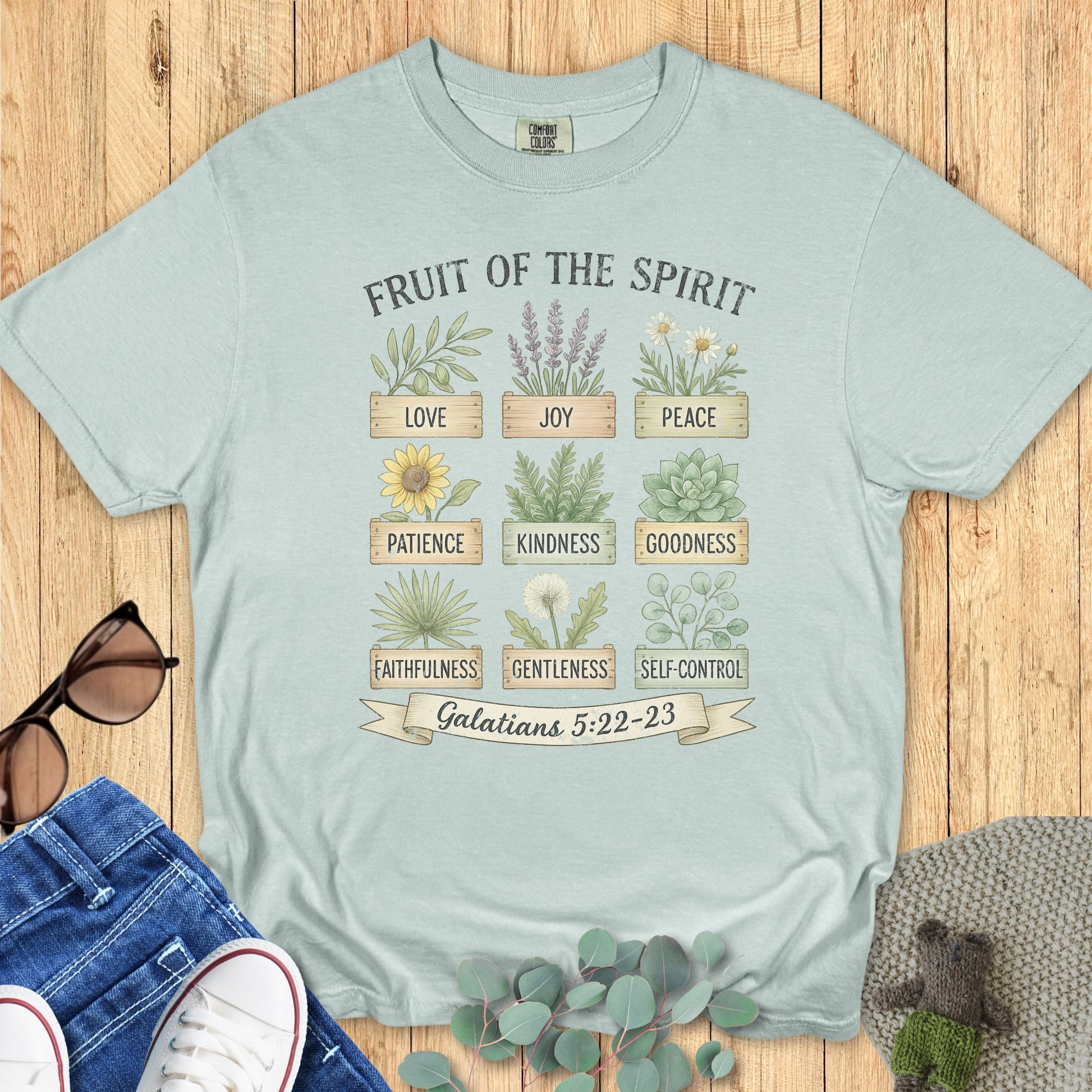 Flatlay of a Comfort Colors 1717 bay “Fruit of the Spirit” t-shirt with a nature-inspired design of herbs and flowers symbolizing Galatians 5:22–23. A fresh women’s scripture tee — faith-based apparel for women and modern Christian shirt, meaningful Christian mom gift idea