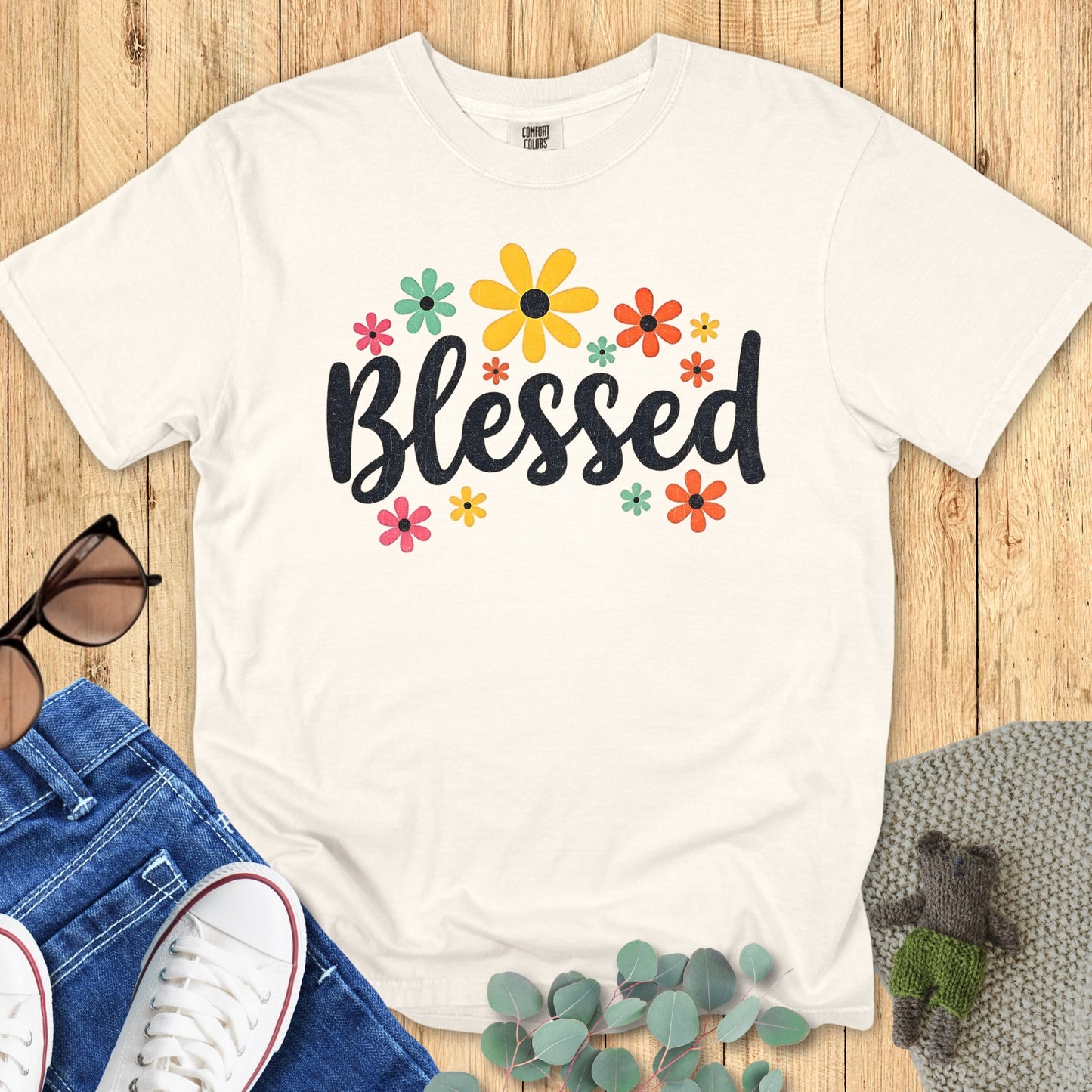 Flatlay of a Comfort Colors 1717 ivory “Blessed” t-shirt with bright floral accents and joyful typography. A soft women’s scripture tee — faith-based apparel for women and modern Christian shirt, thoughtful Christian mom gift idea.