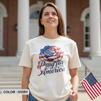 Woman standing proudly outdoors holding an American flag while wearing a Comfort Colors 1717 ivory “Pray for America” t-shirt. A meaningful women’s scripture tee — faith-based apparel for women and modern Christian shirt, uplifting Christian mom gift idea.