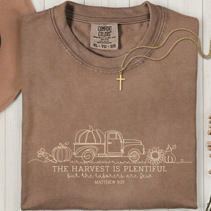 Folded Comfort Colors 1717 espresso “The harvest is plentiful but the laborers are few” t-shirt (Matthew 9:37) with gold cross necklace on top. A rustic women’s scripture tee - faith-based apparel for women and modern Christian shirt, cozy Christian mom gift idea for autumn.