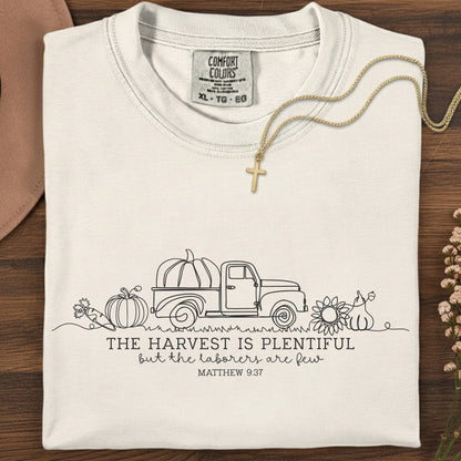 Folded Comfort Colors 1717 ivory “The harvest is plentiful but the laborers are few” t-shirt (Matthew 9:37) styled with gold cross necklace. A neutral women’s scripture tee -  faith-based apparel for women and modern Christian shirt, timeless Christian mom gift idea for the season.
