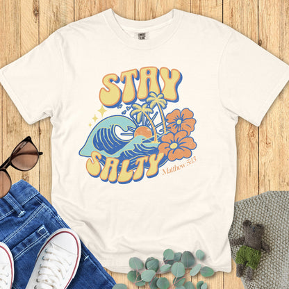 Flatlay of a Comfort Colors 1717 ivory “Stay Salty” t-shirt featuring vintage surf-style art with waves, sun, and hibiscus flowers inspired by Matthew 5:13. A cheerful women’s scripture tee - faith-based apparel for women and modern Christian shirt, perfect Christian mom gift idea for everyday faith and joy.