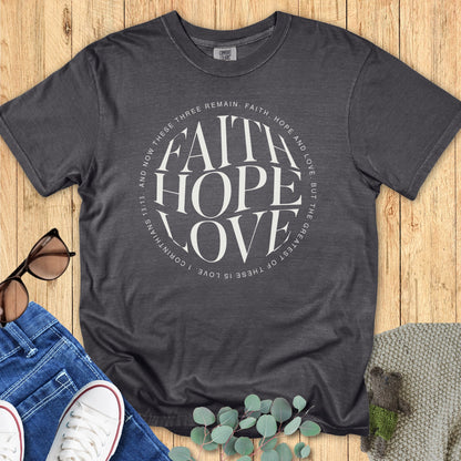 Flatlay of a Comfort Colors 1717 pepper “Faith Hope Love” t-shirt with minimalist typography of 1 Corinthians 13:13. A stylish women’s scripture tee - faith-based apparel for women and modern Christian shirt, thoughtful Christian mom gift idea inspired by biblical love.
