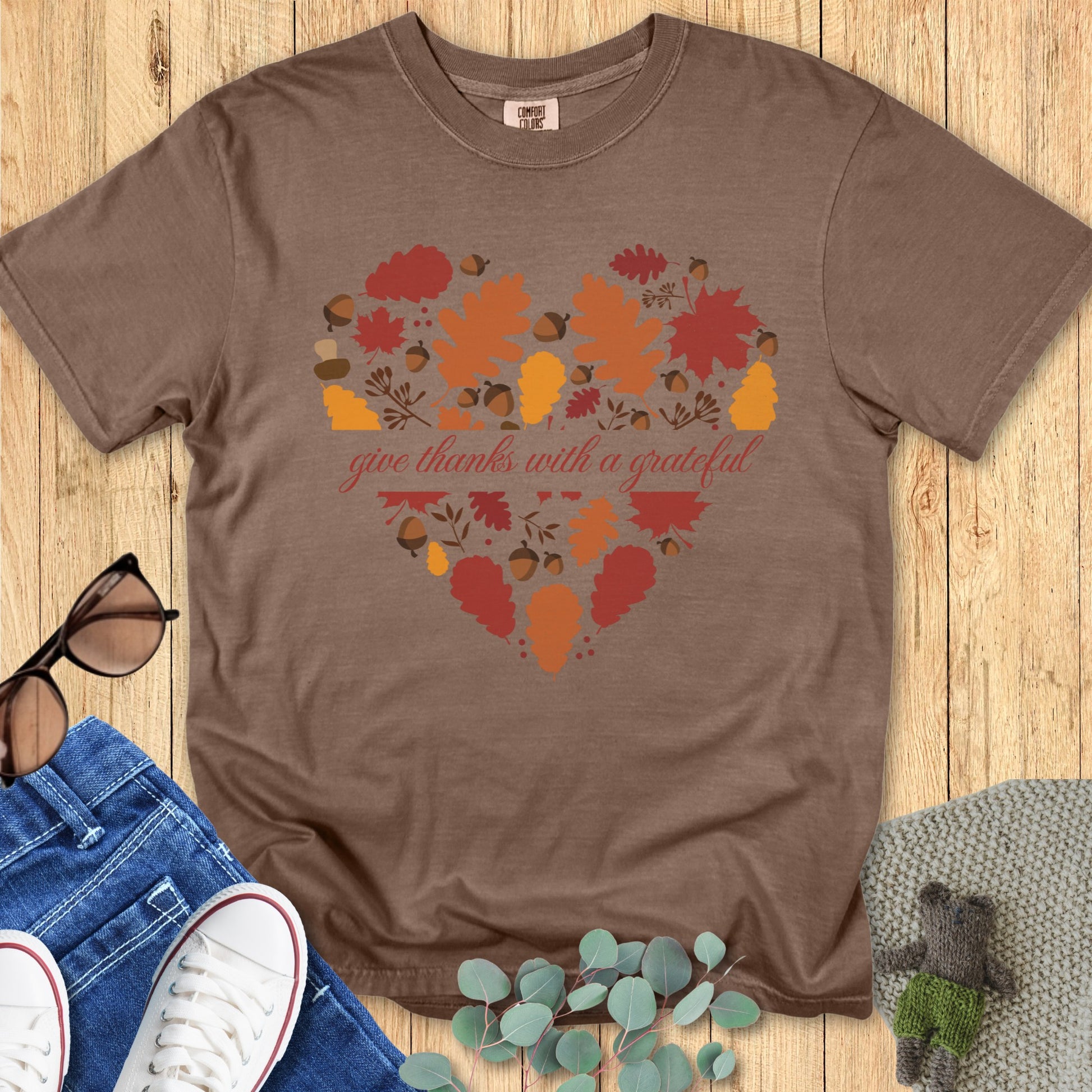 latlay of a Comfort Colors 1717 espresso “Give Thanks with a Grateful Heart” t-shirt with heart-shaped autumn leaf design. A cozy women’s scripture tee - faith-based apparel for women and modern Christian shirt, perfect Christian mom gift idea for showing gratitude this fall.