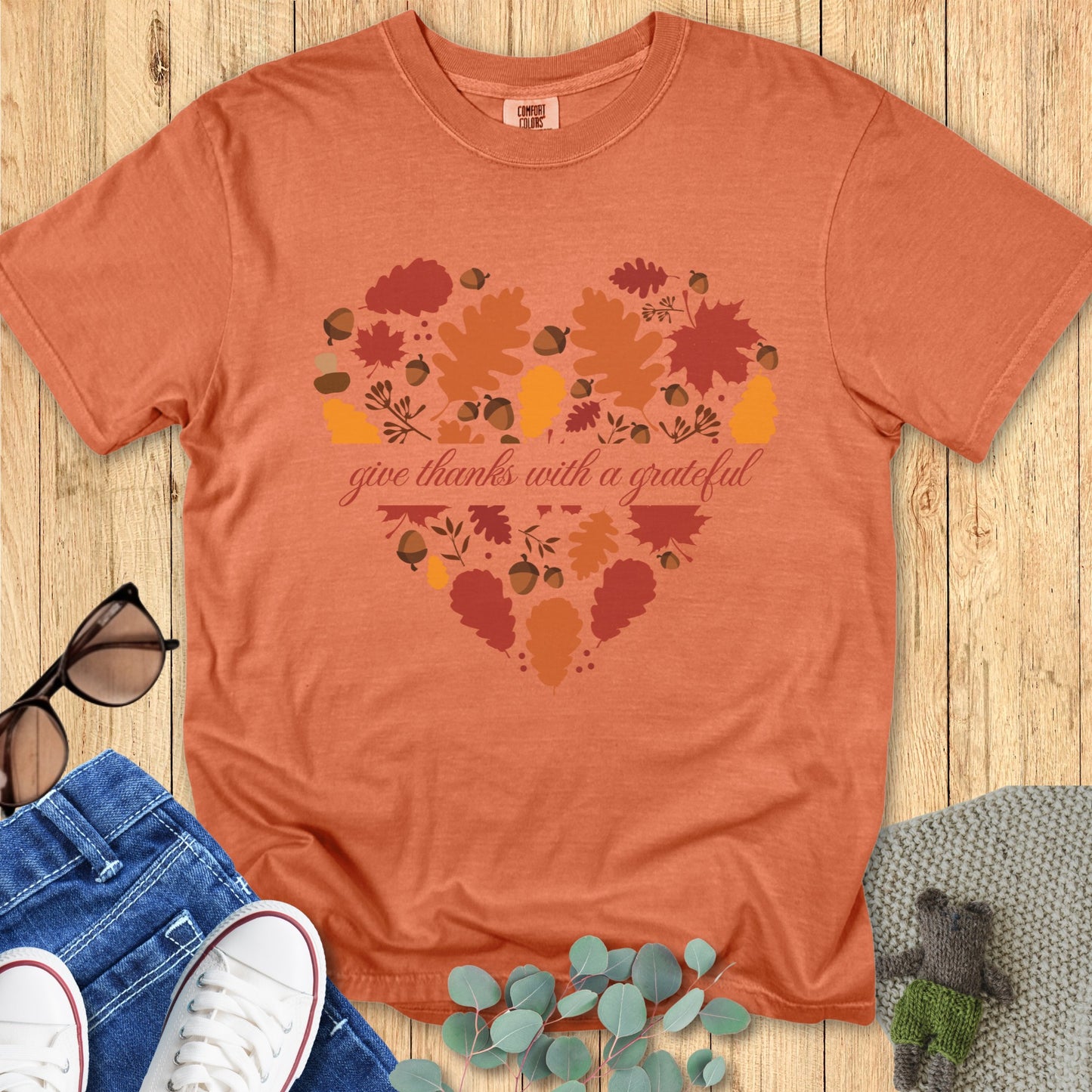 Flatlay of a Comfort Colors 1717 yam “Give Thanks with a Grateful Heart” t-shirt featuring a heart made of fall leaves and acorns. A warm women’s scripture tee - faith-based apparel for women and modern Christian shirt, thoughtful Christian mom gift idea for Thanksgiving or autumn days.