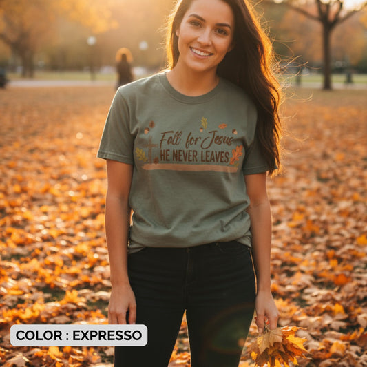 Woman wearing a Comfort Colors 1717 espresso “Fall for Jesus, He Never Leaves” t-shirt surrounded by golden autumn leaves. A seasonal women’s scripture tee -  faith-based apparel for women and modern Christian shirt, thoughtful Christian mom gift idea celebrating faith and fall.