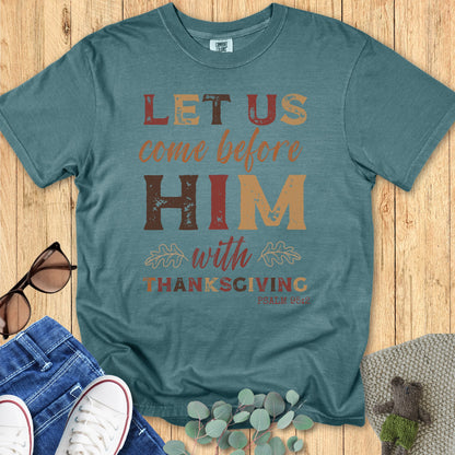 Blue spruce Christian t-shirt flat lay with the Bible verse “Let Us Come Before Him With Thanksgiving, Psalm 95:2.” Distressed fall lettering, leaf accents, rustic Thanksgiving Christian shirt for women, Comfort Colors fall outfit style.
