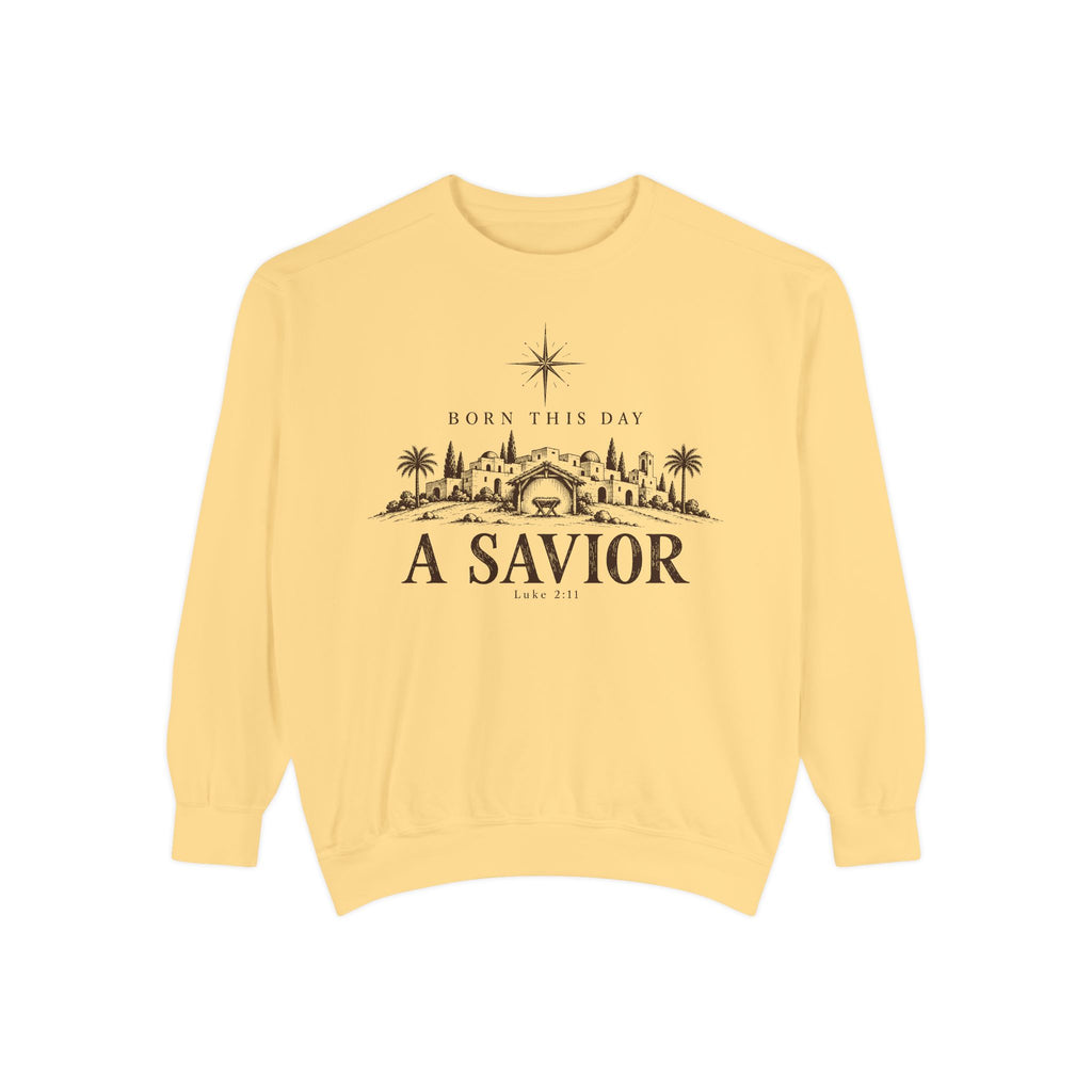 Butter Christian Christmas sweatshirt with Born This Day A Savior lettering, a star over a Bethlehem town scene, a manger and Luke 2:11.