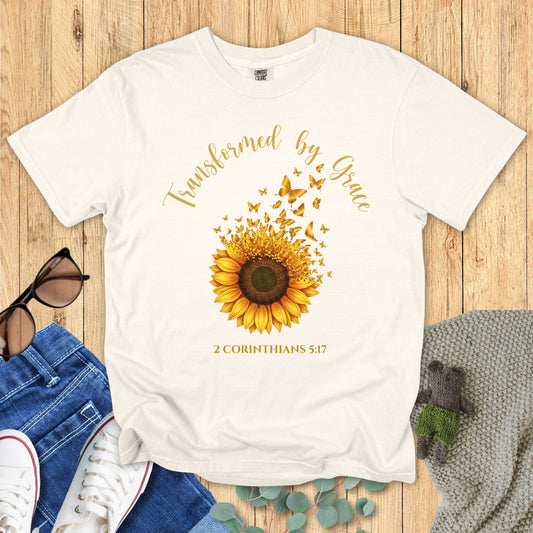Ivory t-shirt with sunflower graphic and text on a wooden surface with accessories.