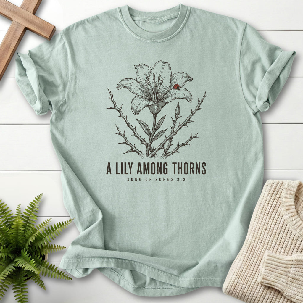 Flat lay of a Bay Christian graphic tee featuring flower artwork with "A Lily Among Thorns T-Shirt" Songs 2:2.
