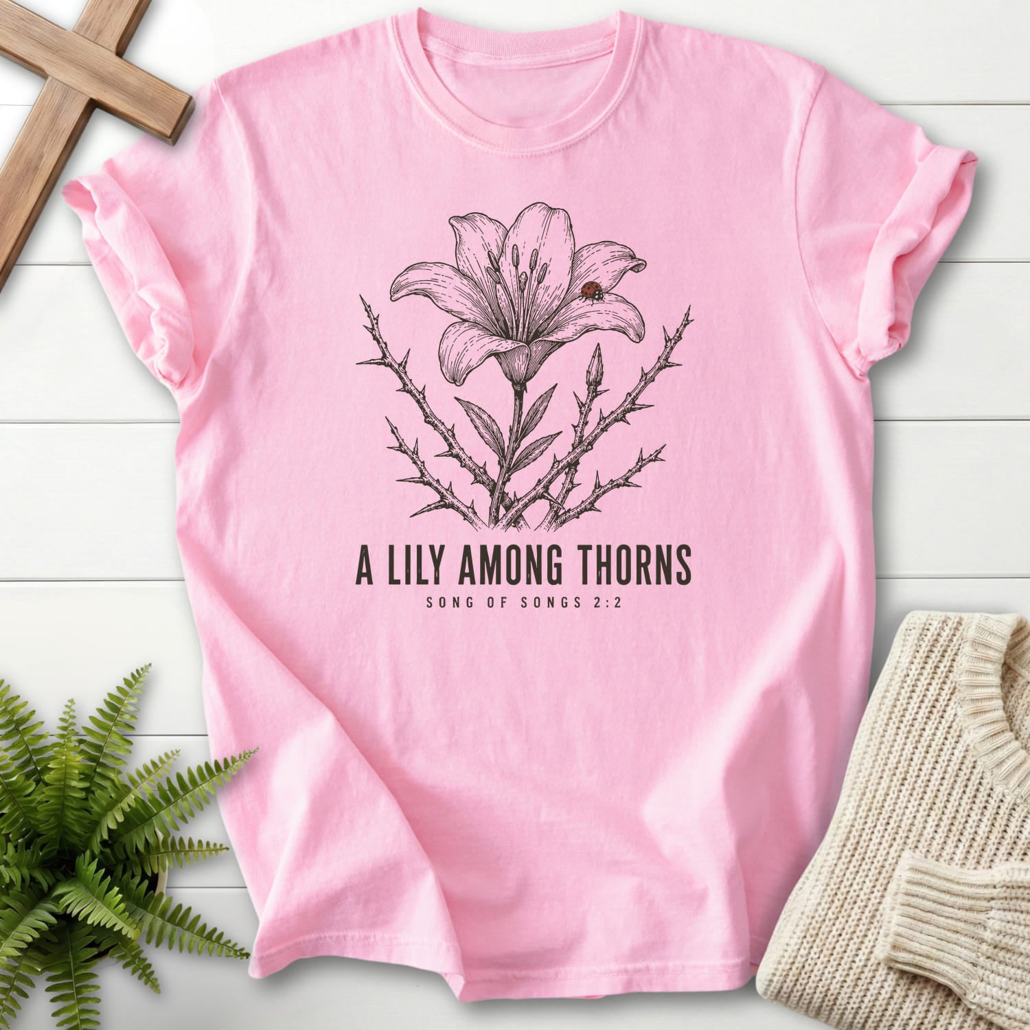 Flatlay of a Blossom Comfort Colors 1717 women's Christian tee with flower artwork with "A Lily Among Thorns T-Shirt" Songs 2:2.