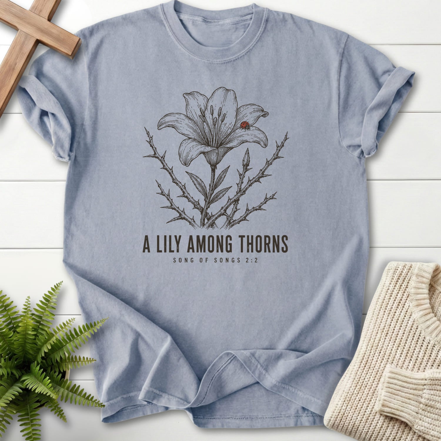 Flat lay of a Granite Christian shirt featuring flower artwork with "A Lily Among Thorns T-Shirt" Songs 2:2.