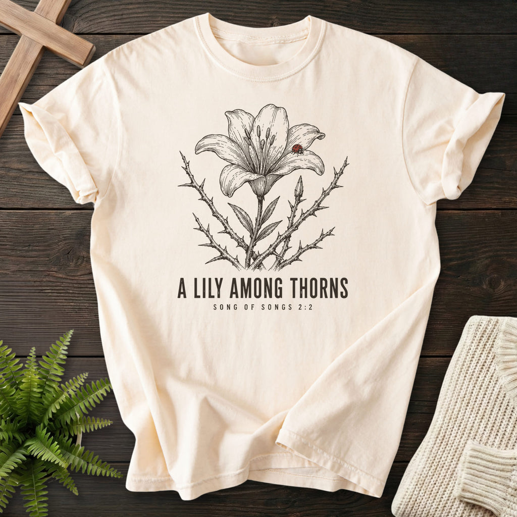 Flatlay of an Ivory Christian t-shirt for women with flower artwork with "A Lily Among Thorns T-Shirt" Songs 2:2.