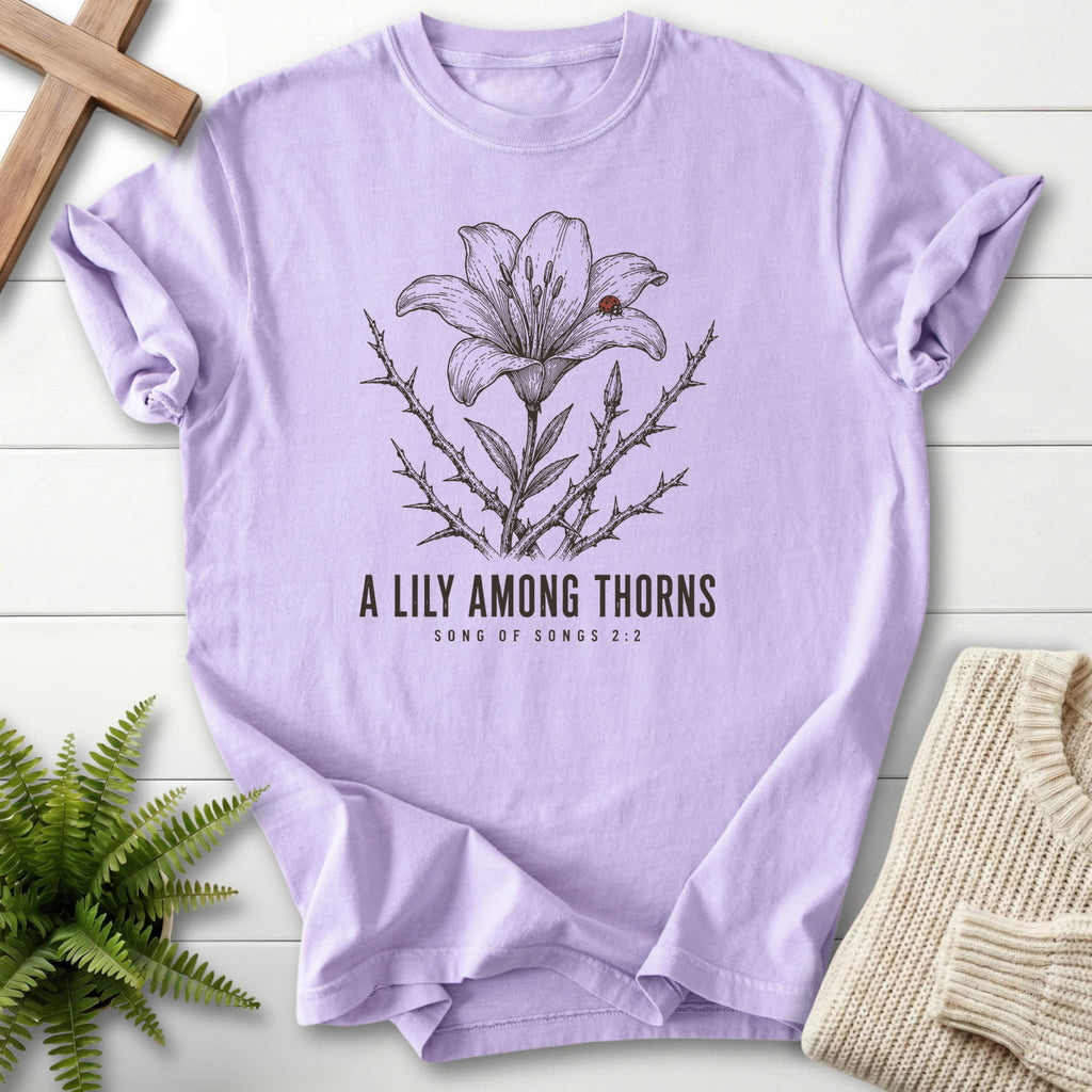 Flat lay of an Orchid Scripture shirt featuring flower artwork with "A Lily Among Thorns T-Shirt" Songs 2:2.