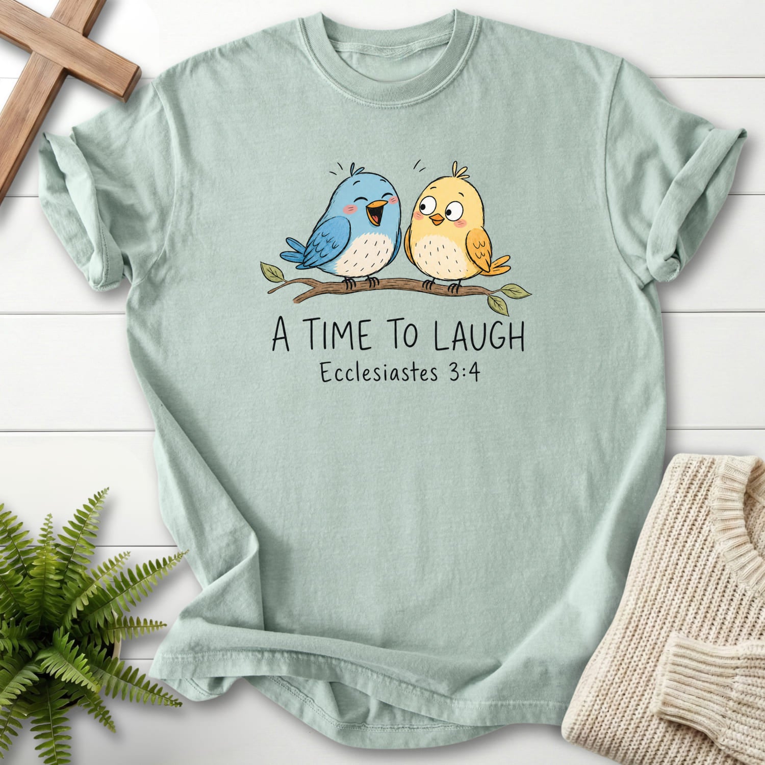 Flat lay of a Bay faith-based tee featuring "A Time To Laugh Faith Birds T-Shirt" Ecclesiastes 3:4.