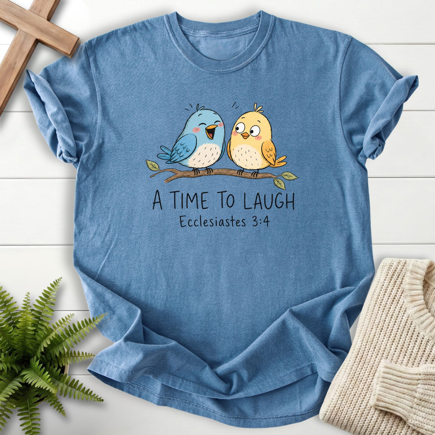 Flatlay of a Blue Jean Scripture shirt with "A Time To Laugh Faith Birds T-Shirt" Ecclesiastes 3:4.