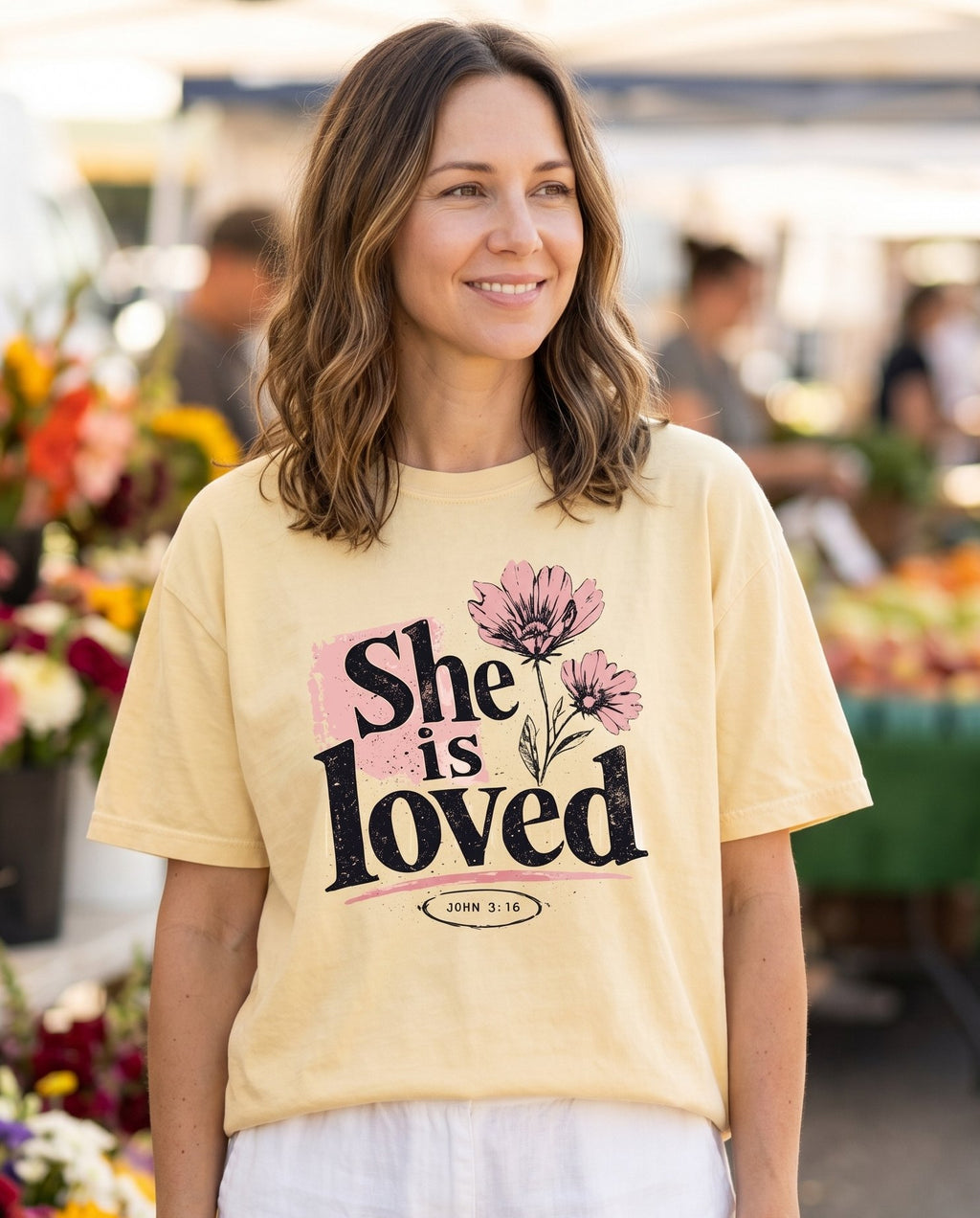 She Is Loved – Banana women's Christian tee, lifestyle photo in farmers market – She Is Loved floral flowers botanical faith beloved encouragement desi – She Wears Faith