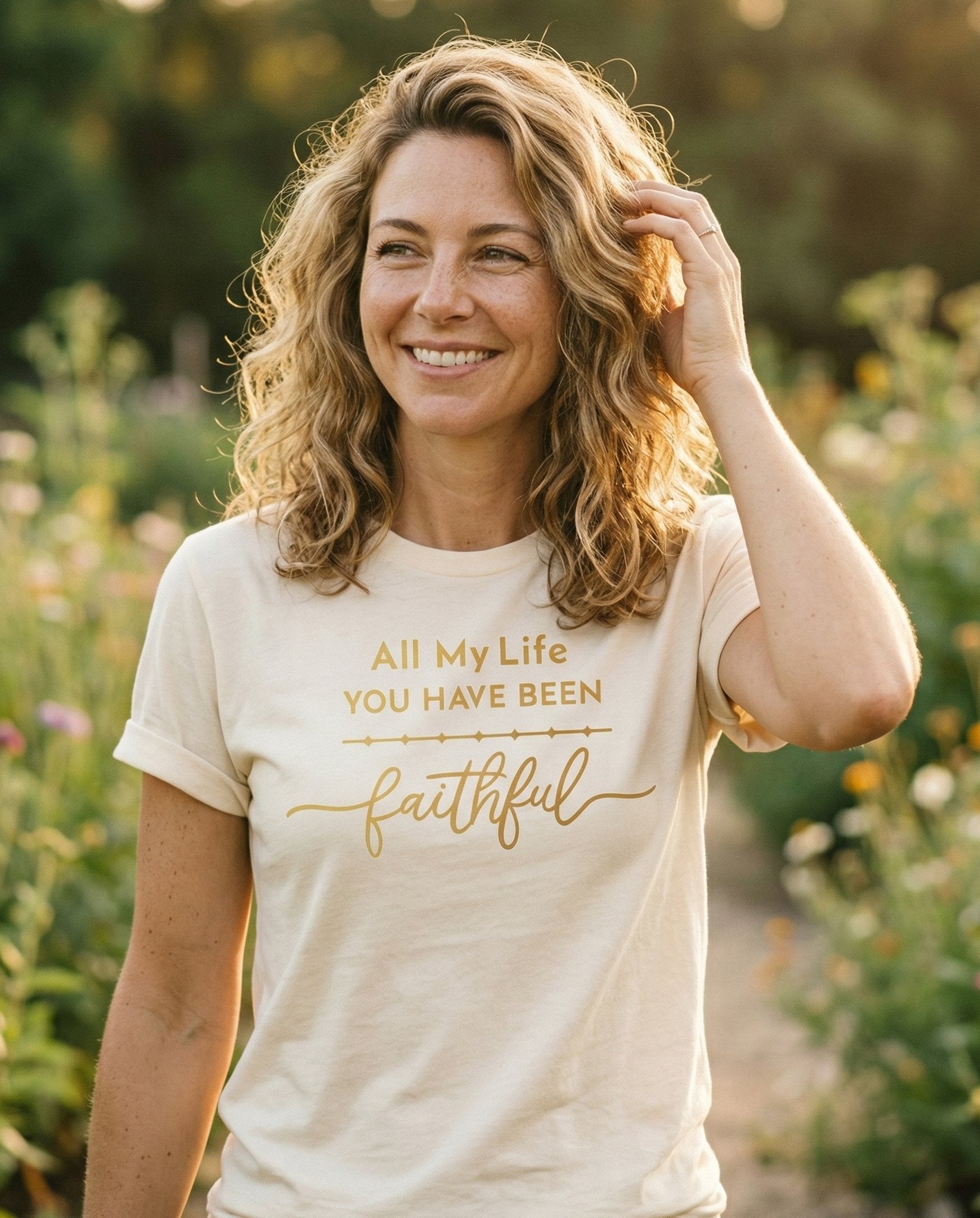 All My Life – Ivory women's Christian tee, lifestyle photo in outdoor garden – Gold script lettering reads 'All My Life YOU HAVE BEEN faithful' with  – She Wears Faith