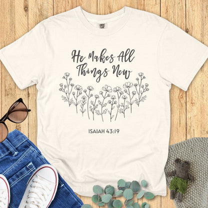 Comfort Colors 1717 Christian women t-shirt in ivory flat lay. Design features the phrase “He Makes All Things New – Isaiah 43:19” above delicate black floral line art